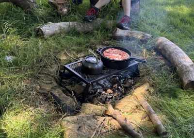 Picture of a pizza cooking in a cast iron pan over a man made fire pit